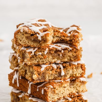 A stack of five Cinnamon Roll Blondies drizzled with glaze. The blondie on top has a bite taken out of it.